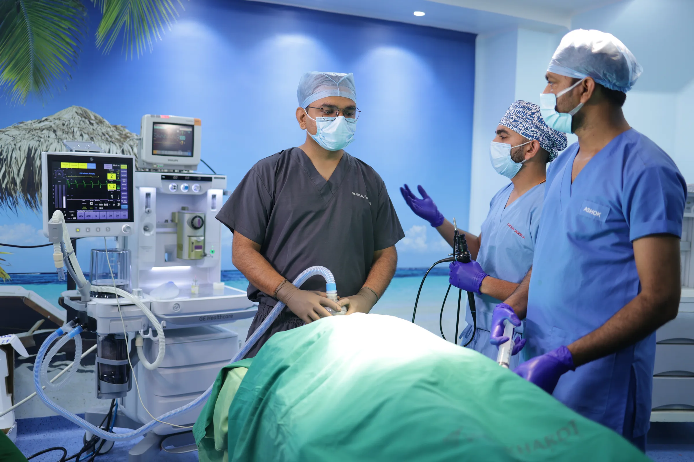 An anaesthetist holding the breathing circuit while a colleague holds a flexible endoscope. The patient is covered by surgical drapes.
