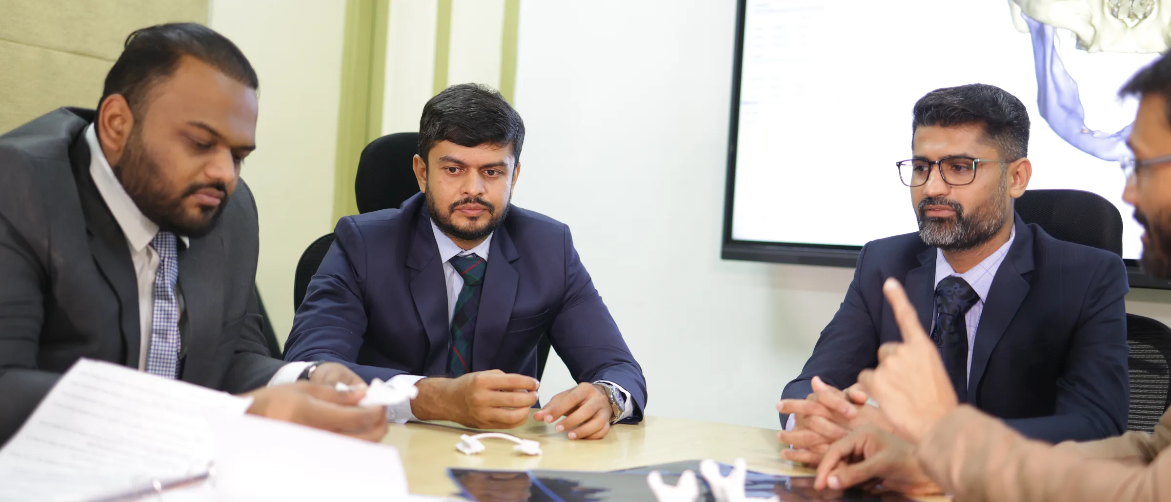 Four of the practice's surgeons round the tumour board table, 3D-printed jaw segments and scan films in front of them and the CT reconstruction they were made from on the screen behind.