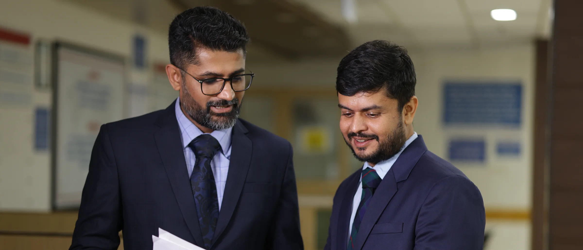 Two of the practice's cancer surgeons in the OPD, reading the same open case file with the pages fanned between them.