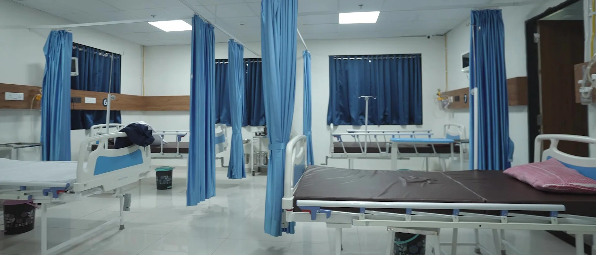 An empty ward bay, beds made and the curtains drawn back.