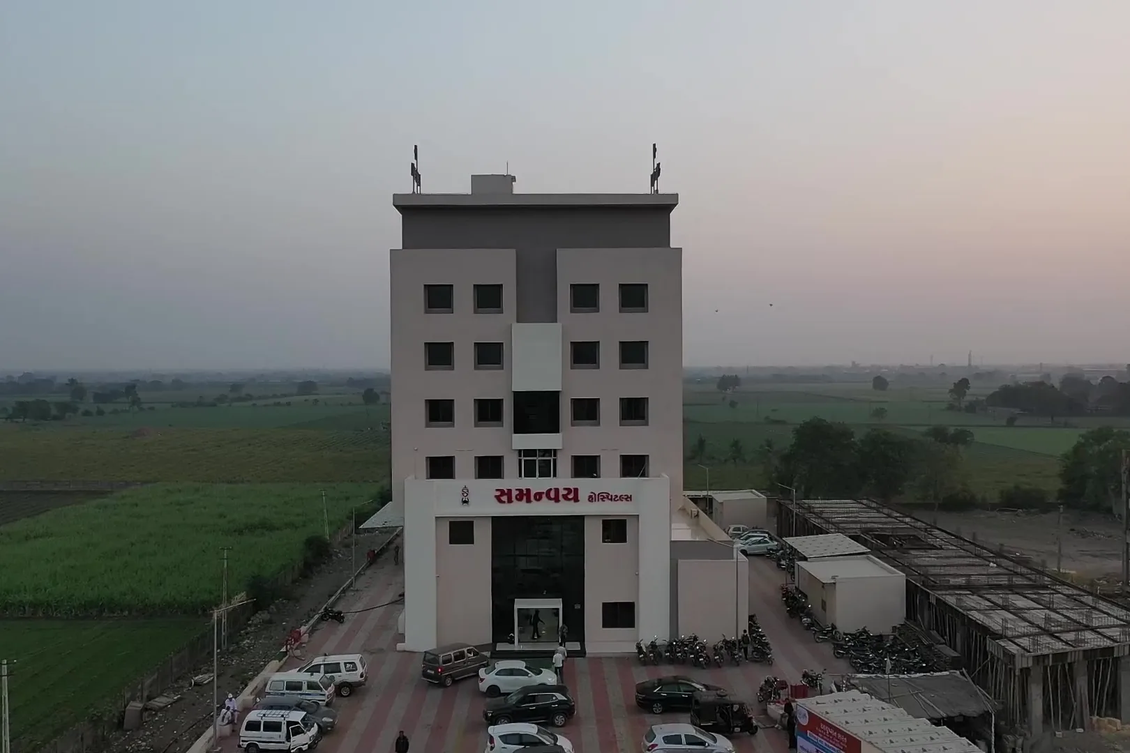 Samanvay Hospital in Junagadh seen from above, the building standing among open farmland.