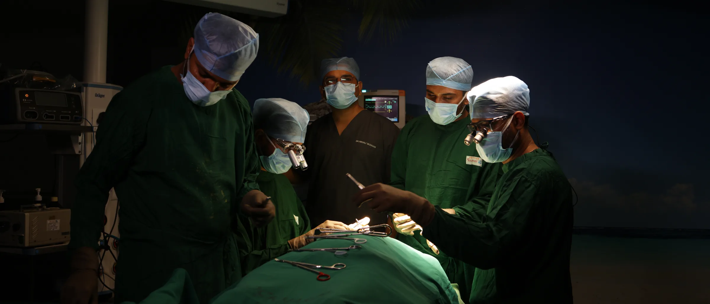 Five of the theatre team round a draped patient, surgical clamps laid out on the drape and an instrument being passed.