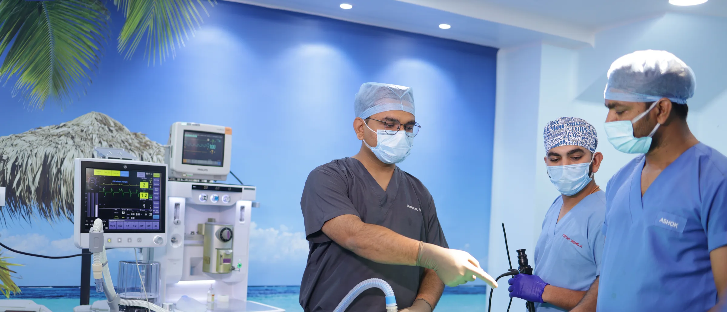 An anaesthetist reaching towards a flexible endoscope held by a colleague beside the anaesthetic machine.