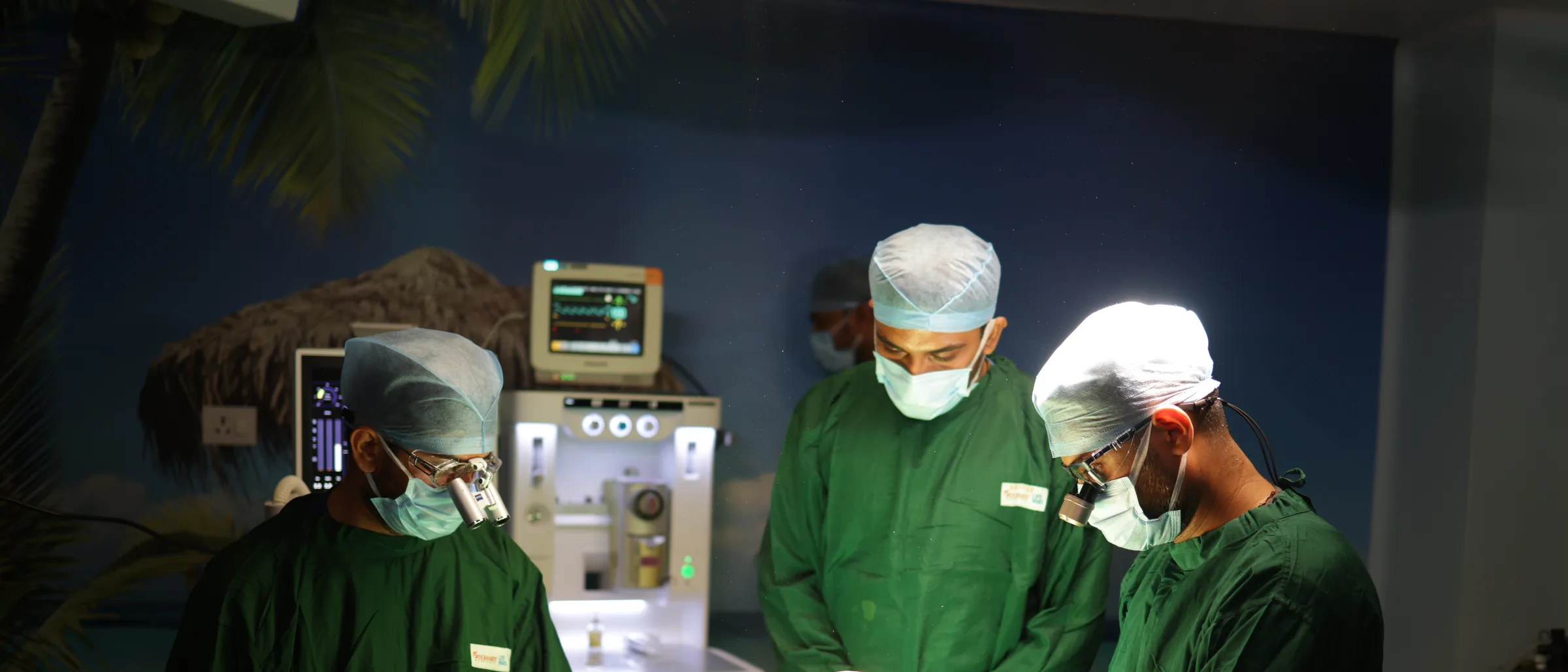 Three gowned surgeons at the operating table beside the anaesthetic machine and the vitals monitor.