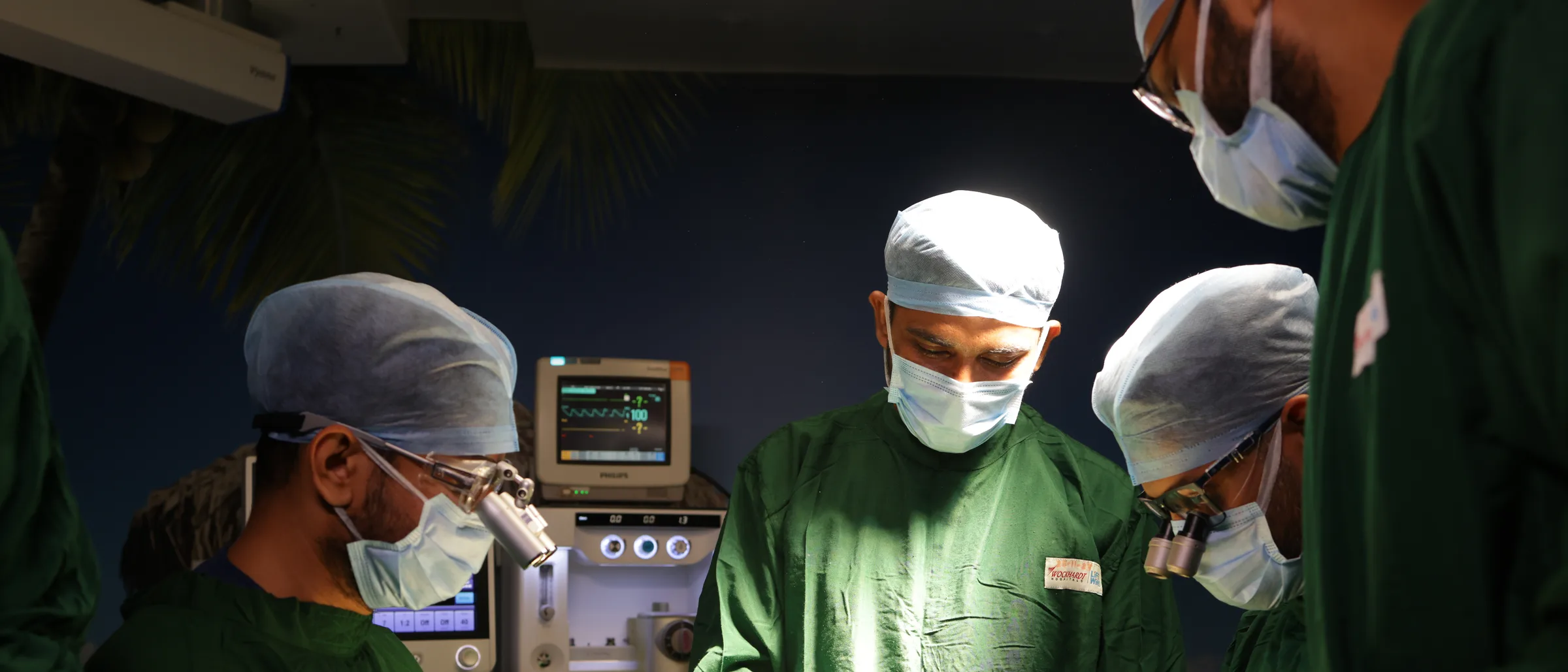 Four of the theatre team at work with the patient's vitals monitor lit behind them.