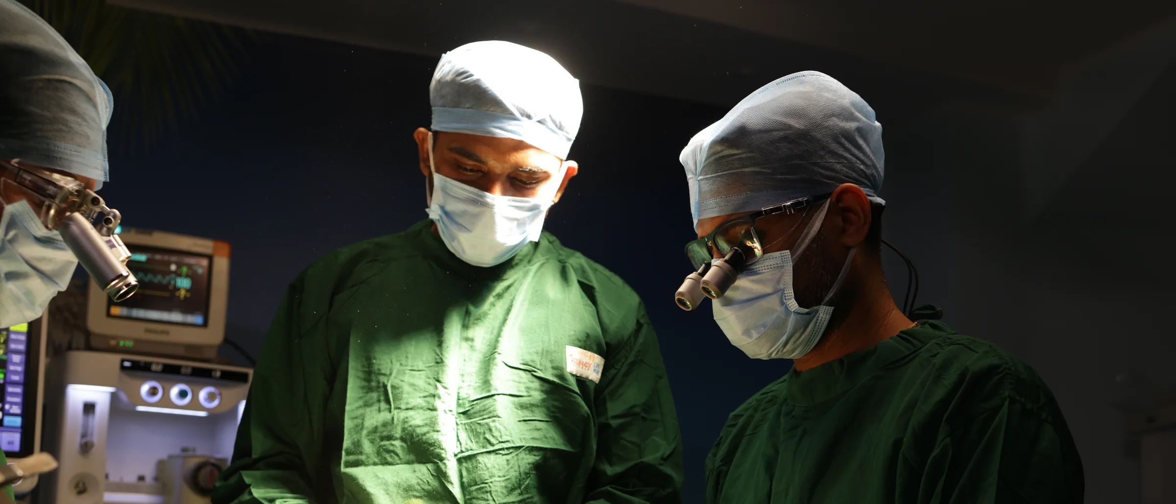 Two surgeons in gowns and masks, one wearing loupes, working together over a draped patient.