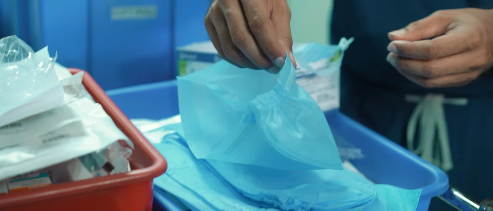 A theatre trolley being set up before an operation: sealed instrument packs laid out on the trays, and a pair of hands opening one of them.