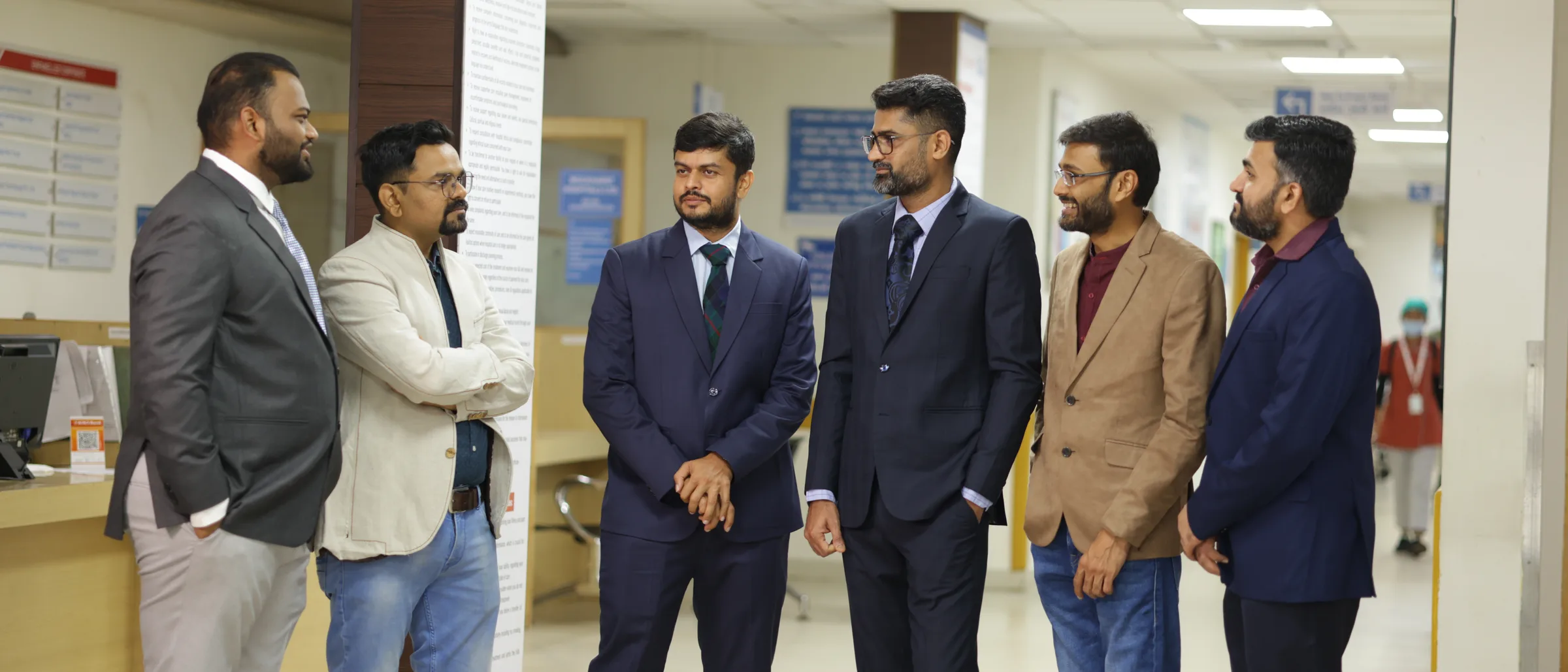 Six of the practice's consultants standing together in the Wockhardt outpatient department, talking, with the billing counter and the corridor behind them.