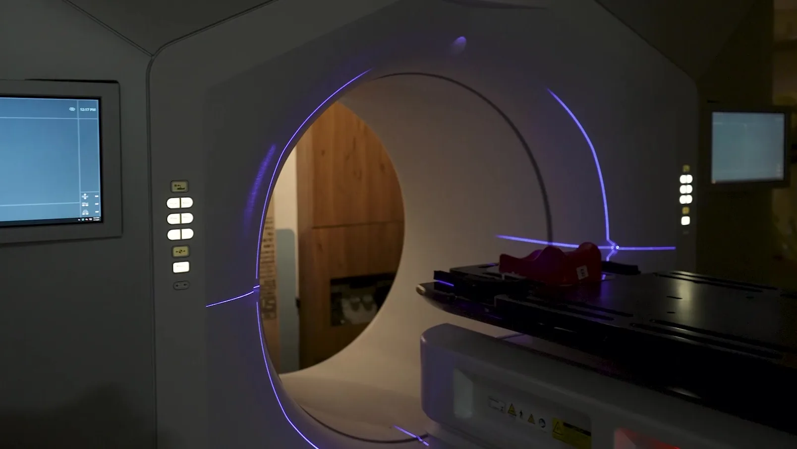 The radiotherapy machine in its treatment room, the ring of it lit and the couch empty.