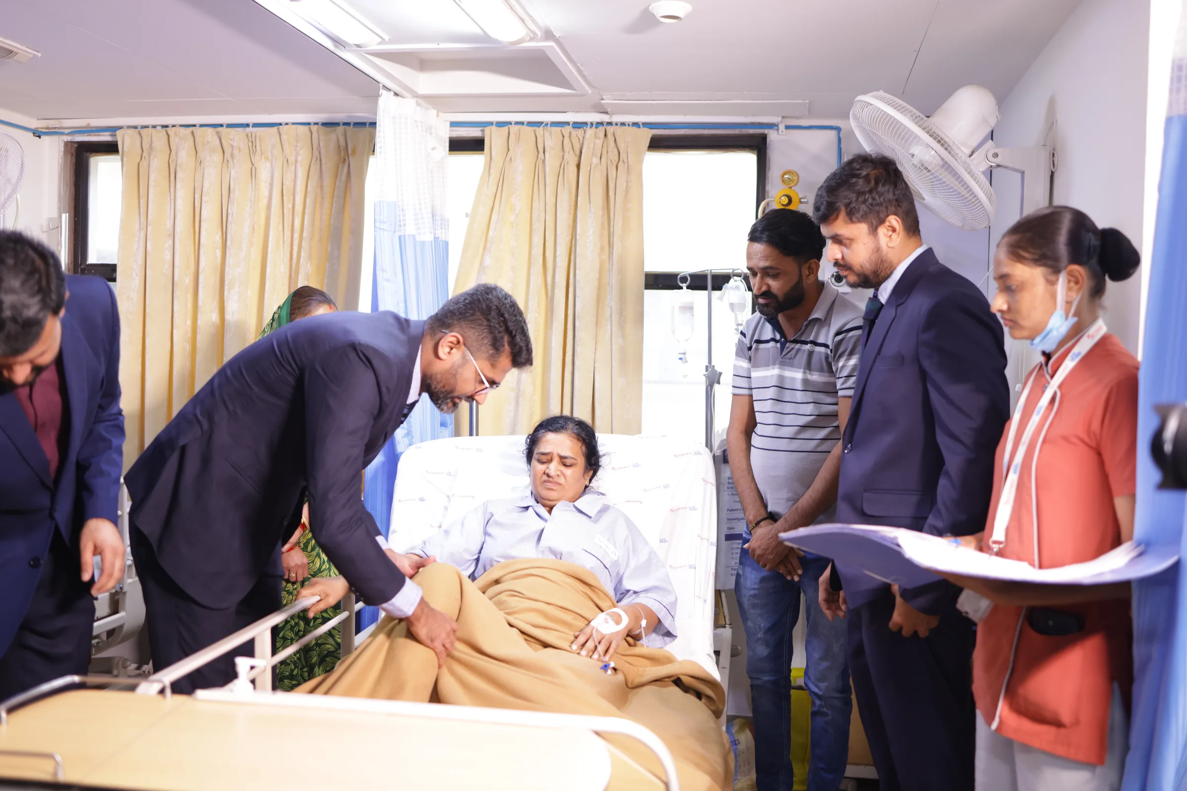 A ward round at a patient's bedside, a relative standing with them as the doctor talks.